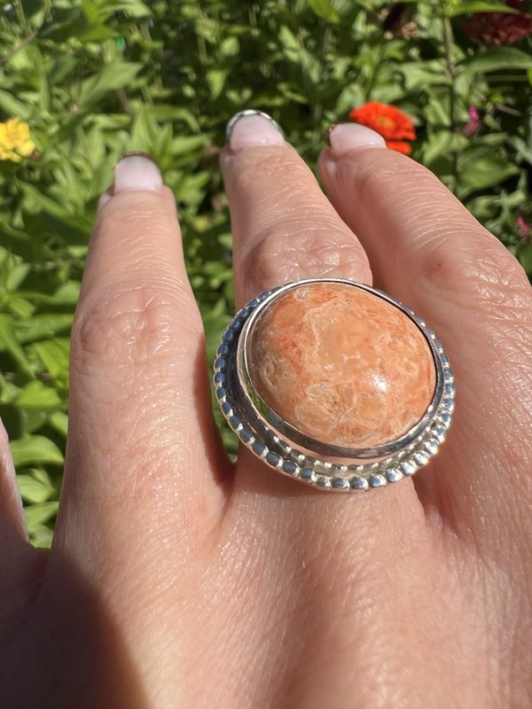 The orange cabochon ring worn on a hand in the garden