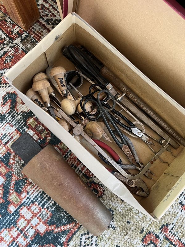 A box of old hand tools, pliers and a mallet, on a rug